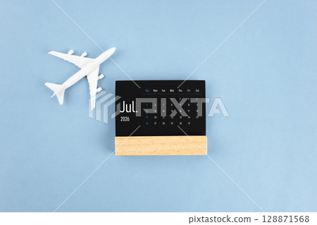 July 2026 black wooden calendar and airplane toy on blue color background. July 2026 black wooden calendar and airplane toy on blue color background. 128871568