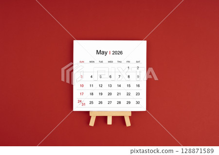 Calendar page for May 2026 with wood easel on a dark red background. 128871589