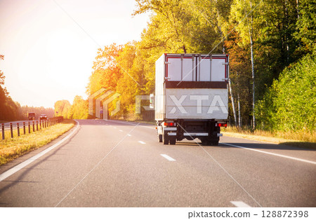 A refrigerated truck transports perishable food cargo along a highway in summer against a sunset backdrop, industry. Copy space for text 128872398