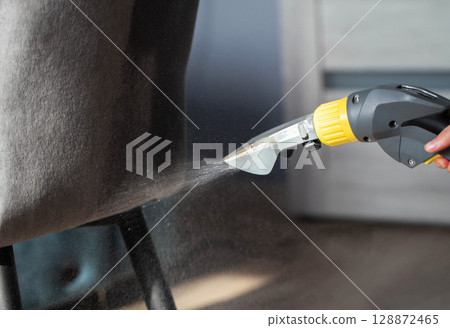Spraying a chemical from a washing vacuum cleaner when cleaning the fabric upholstery of a chair. Cleaning services, industry Spraying a chemical from a washing vacuum cleaner when cleaning the fabric upholstery of a chair. Cleaning services, industry 128872465
