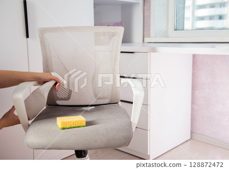 Women's hands wash dirty spots from gray upholstery of computer chair. Concept of dry cleaning of upholstered furniture at home, business, industry Women's hands wash dirty spots from gray upholstery of computer chair. Concept of dry cleaning of upholstered furniture at home, business, industry 128872472