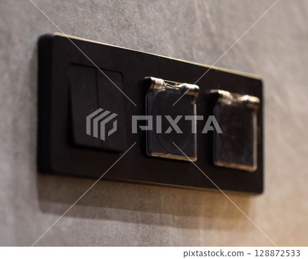 triple closed black socket with switch on gray tiled wall background, close-up triple closed black socket with switch on gray tiled wall background, close-up 128872533