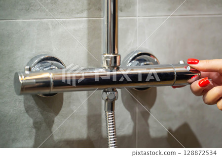 Women's fingers with red manicure regulate the water temperature in the shower tap, close-up Women's fingers with red manicure regulate the water temperature in the shower tap, close-up 128872534