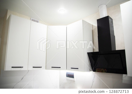 Black modern kitchen range hood against white kitchen cabinets, close-up 128872713