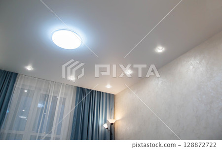 Modern stylish ceiling with diode chandelier and spotlights in the room and turquoise curtains. Copy space for text 128872722