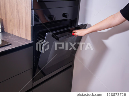 A woman's hand opens a modern stylish built-in catalytic oven for automatic cooking. Stylish interior 128872726
