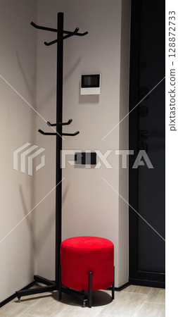 Modern red pouf in hallway corner for sitting against clothes rack background, interior Modern red pouf in hallway corner for sitting against clothes rack background, interior 128872733