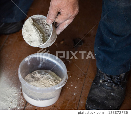 Dolomite flour in a mug against the background of a bucket, fertilizing the soil at the dacha, close-up Dolomite flour in a mug against the background of a bucket, fertilizing the soil at the dacha, close-up 128872786