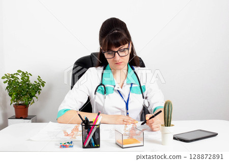 Beautiful girl gynecologist doctor in glasses in the office. Concept of examination of female patients. Copy space for text, diagnostic Beautiful girl gynecologist doctor in glasses in the office. Concept of examination of female patients. Copy space for text, diagnostic 128872891