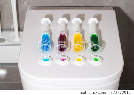 A set of multi-colored syringes with different scents on the toilet bowl in the toilet for cleaning and disinfection. Hygiene and antibacterial effect, close-up A set of multi-colored syringes with different scents on the toilet bowl in the toilet for cleaning and disinfection. Hygiene and antibacterial effect, close-up 128872912