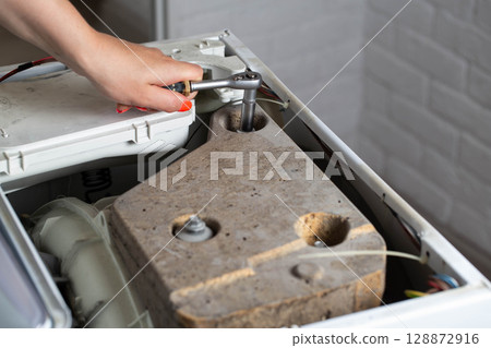 A washing machine repairman tightens the counterweight in the washing machine due to noise and vibration. Copy space for text 128872916
