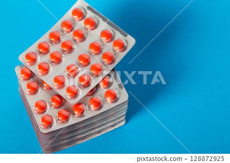 Stack of red pills on blue background. Concept of treatment with antibiotics tetracyclines in medicine. Copy space for text Stack of red pills on blue background. Concept of treatment with antibiotics tetracyclines in medicine. Copy space for text 128872925