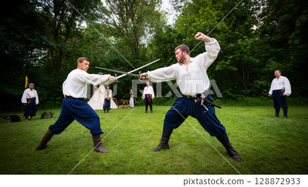 Sword Fighting Demonstration by Historical Reenactors in a Lush Green Forest Setting 128872933
