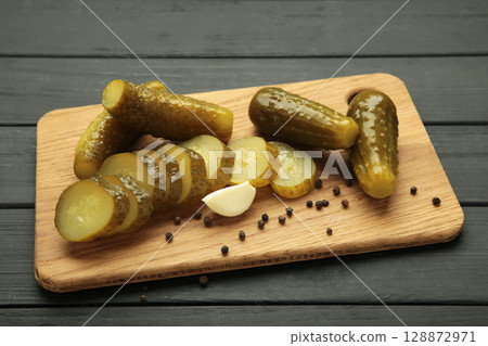 Marinated pickled cucumber on cutting board on black wooden background. Marinated pickled cucumber on cutting board on black wooden background. 128872971