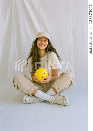 A woman is sitting on the floor with a yellow smiley face ball in her hand A woman is sitting on the floor with a yellow smiley face ball in her hand 128873048