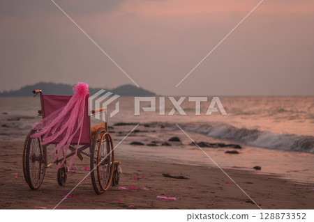 Wheelchair with Wind Blown Ribbon Tied to Handle on Serene Beach at Sunset 128873352