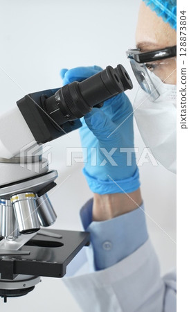 Scientist woman wearing gloves and a mask uses a microscope in a laboratory setting, conducting important research and analysis, close up. Medicine and science concept Scientist woman wearing gloves and a mask uses a microscope in a laboratory setting, conducting important research and analysis, close up. Medicine and science concept 128873804