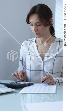 Female professional calculating finances, reviewing paperwork, tracking business expenses with precision and focus. Audit and taxes in business 128873817