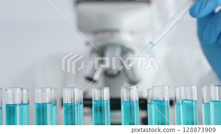 Close up of scientific researcher wearing protective gear, carefully pipetting liquid into test tubes while conducting medical research experiment in laboratory. Medicine, healthcare and science 128873909