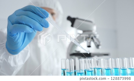 Scientific researcher wearing protective gear, carefully pipetting liquid into test tubes while conducting medical research experiment in laboratory. Medicine, healthcare and science concept Scientific researcher wearing protective gear, carefully pipetting liquid into test tubes while conducting medical research experiment in laboratory. Medicine, healthcare and science concept 128873998