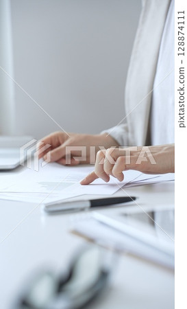 Businesswoman reviewing financial documents and charts, performing data analysis for business planning and decision making in a professional office background. Business people concept Businesswoman reviewing financial documents and charts, performing data analysis for business planning and decision making in a professional office background. Business people concept 128874111