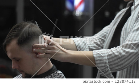 Professional barber carefully combing client's hair, preparing precise hairstyle with expert grooming techniques in modern barbershop setting 128874112