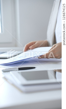 Businesswoman reviewing financial documents and charts, performing data analysis for business planning and decision making in a professional office background. Business people concept Businesswoman reviewing financial documents and charts, performing data analysis for business planning and decision making in a professional office background. Business people concept 128874125