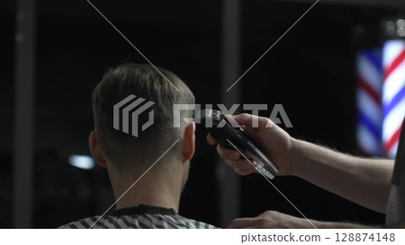 Skilled barber trimming client's hair with electric razor, creating precise contemporary hairstyle inside sleek urban barbershop setting Skilled barber trimming client's hair with electric razor, creating precise contemporary hairstyle inside sleek urban barbershop setting 128874148