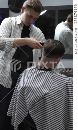 Professional barber carefully trimming customer's hair with electric clipper, providing a stylish and precise haircut in a modern barbershop environment Professional barber carefully trimming customer's hair with electric clipper, providing a stylish and precise haircut in a modern barbershop environment 128874156