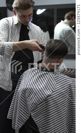 Professional barber carefully trimming customer's hair with electric clipper, providing a stylish and precise haircut in a modern barbershop environment 128874171
