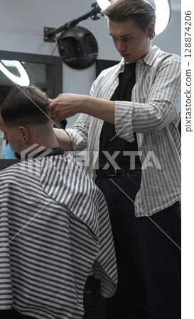 Professional barber carefully trimming customer's hair with electric clipper, providing a stylish and precise haircut in a modern barbershop environment 128874206