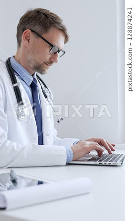 Adult doctor man is typing on a laptop, likely updating patient records or conducting research, showcasing the intersection of healthcare and technology in medical setting. Medicine concept Adult doctor man is typing on a laptop, likely updating patient records or conducting research, showcasing the intersection of healthcare and technology in medical setting. Medicine concept 128874241