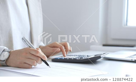 Businesswoman is calculating annual tax using calculator and taking notes in the office, managing domestic budget and checking financial documents. Audit and taxes in business Businesswoman is calculating annual tax using calculator and taking notes in the office, managing domestic budget and checking financial documents. Audit and taxes in business 128874422