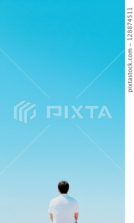 Businessman sitting against expansive blue sky, experiencing moment of reflection, embodying personal freedom and contemplating boundless life opportunities during bright sunny day 128874511