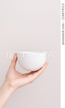 Woman hand gripping pristine white ceramic bowl, positioned against soft pastel background, highlighting culinary minimalism and product presentation potential 128874513