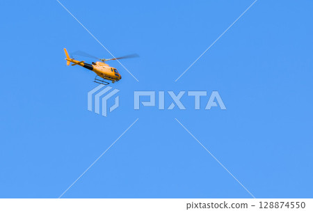 A helicopter soaring through a bright blue sky. 128874550