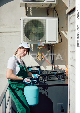 Woman technician maintaining rooftop air conditioning system outdoors 128875999