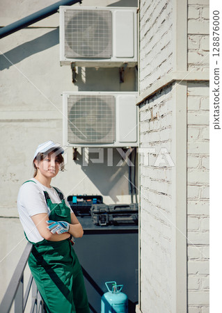 Uniformed HVAC technician beside outdoor air conditioning units 128876000