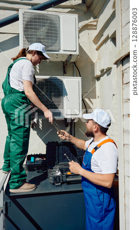 Technicians working together to install rooftop air conditioning unit 128876003