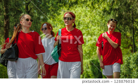 Women football team walking confidently in park with red jerseys and sunglasses Women football team walking confidently in park with red jerseys and sunglasses 128876018