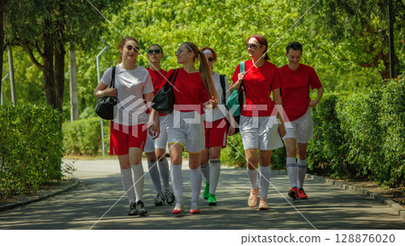 Women football team walking confidently on sunny path in park 128876020