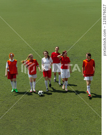 Young women football players on grass field holding soccer ball 128876027
