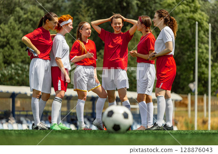 Women football team in red jerseys huddling on sunny green field 128876043