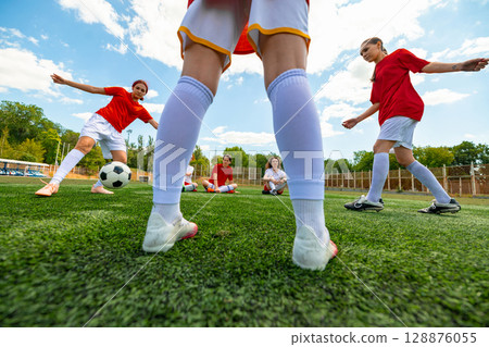 Women football players practicing on sunny green field during daytime match 128876055
