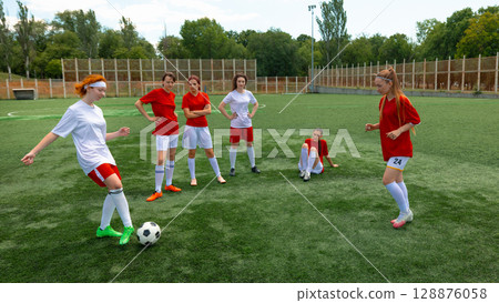 Women soccer squad training on grassy athletic field beneath cloudless sky 128876058
