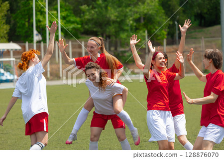 Female soccer players celebrate their teamwork on a sunny day outside 128876070