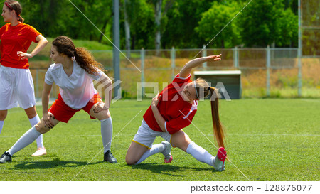 Female football athletes stretching on a sunny day on a grassy field 128876077