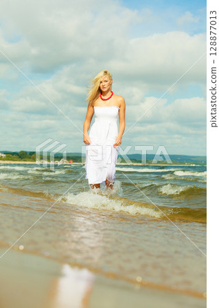 Blonde woman wearing dress walking in water 128877013