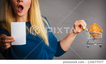 Shocked woman holding shopping basket with bread Shocked woman holding shopping basket with bread 128877077