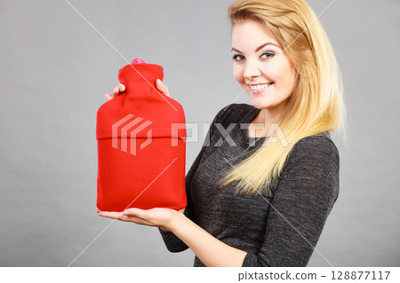Happy woman holds hot water bottle 128877117
